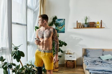 Genç, yakışıklı bir adam pencerede duruyor, telefonunu tutuyor ve gün ışığının tadını çıkarıyor..