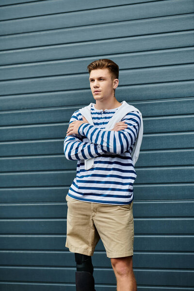 Молодой, красивый мужчина стоит с уверенностью, скрестив руки, демонстрируя свою протезную ногу.