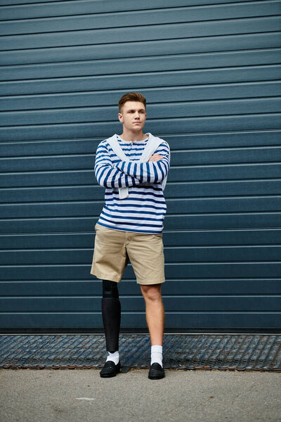 Молодой человек со скрещенными руками показывает свою протезную ногу на современном фоне.