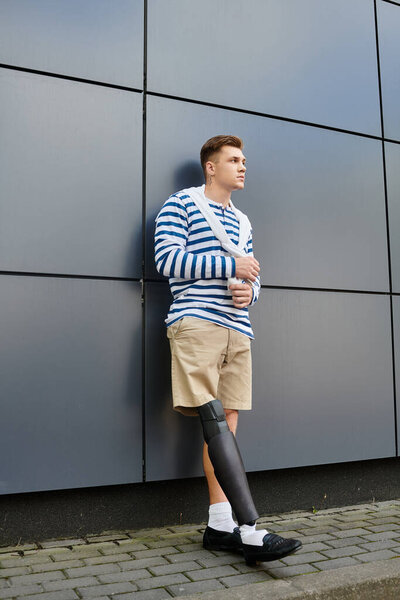 Красивый молодой человек уверенно стоит у современного здания, демонстрируя свою протезную ногу..