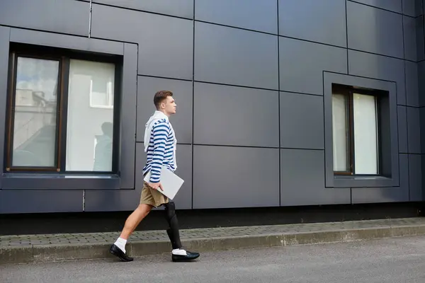 stock image A young man in a striped shirt and shorts walks by a modern building.