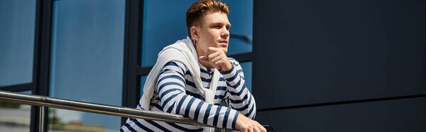 Молодой, красивый мужчина задумчиво покоится на перилах в яркой городской обстановке..