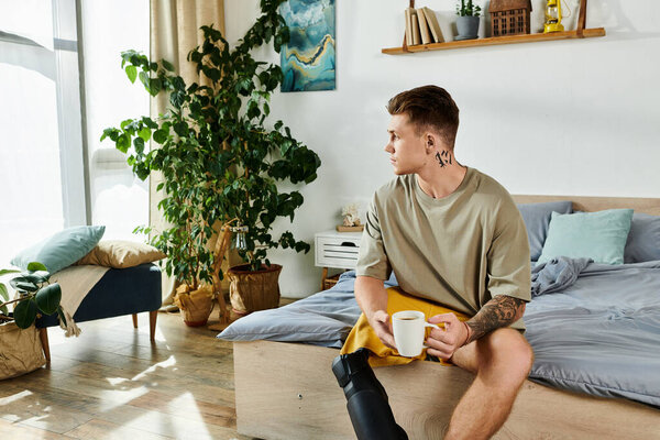 Молодой человек сидит задумчиво на своей кровати, держа чашку, окруженный зеленью и солнечным светом.
