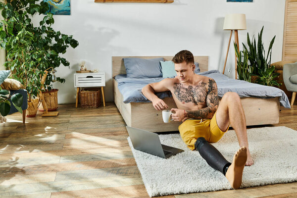 Молодой красивый мужчина расслабляется в своей комнате, потягивая кофе и комфортно работая над ноутбуком..