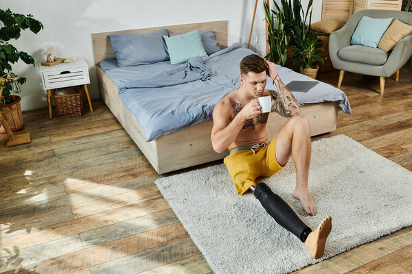 Молодой человек расслабляется на полу, потягивая кофе, демонстрируя протезы ног и татуировки..
