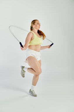 A determined woman in a crop top jumps rope in a well-lit studio, embodying strength and fitness. clipart