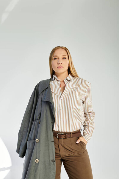 Потрясающая женщина в осенней манере уверенно позирует в студии на сером фоне.