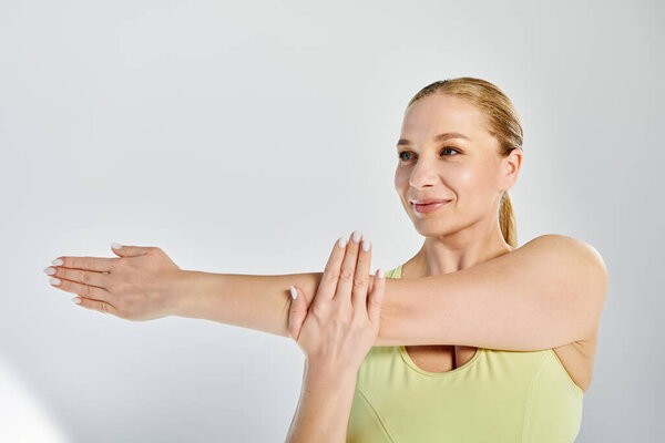 A dedicated woman in a crop top is stretching her arms in a bright studio setting to enhance her workout routine.