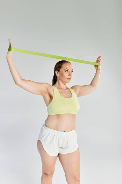 Решительная женщина упражняется с группой сопротивления в ярко освещенной студии, демонстрируя свою силу и сосредоточенность.