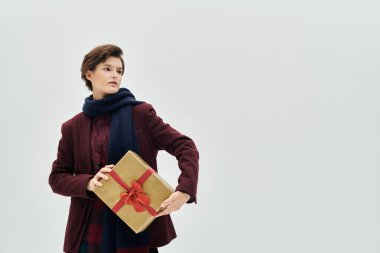 Zengin kış renkleri giymiş şık bir kadın bol özenle sarılmış bir hediye sunar.