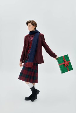 Rahat kış kıyafetleri içinde şık bir kadın huzurlu bir ortamda bir hediyeyle zarifçe poz verir..