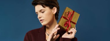 Kış modasında zarif bir kadın kırmızı kurdeleli altın bir hediye kutusuyla zarifçe poz verir..