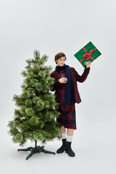 Прекрасная женщина в уютной зимней моде держит подарок у елки.