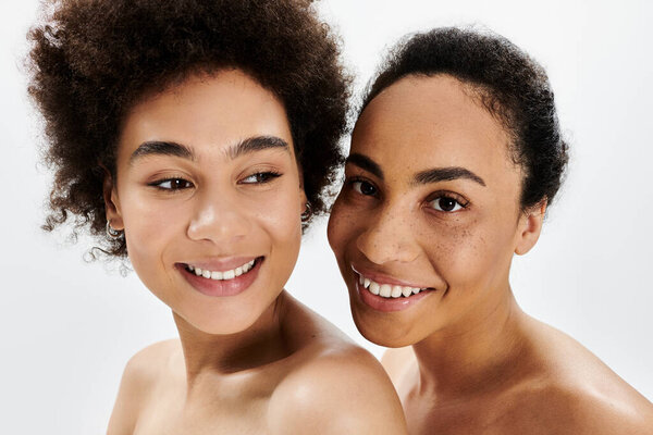 Two women share joyful smiles, showcasing natural beauty and warmth in their expressions.