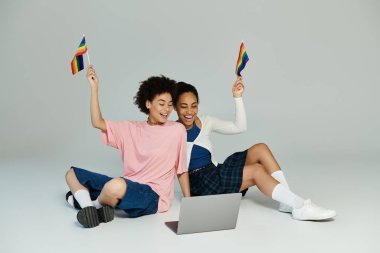 İki arkadaş, bir bilgisayarla uğraşırken sevinçle renkli bayraklar sallarken heyecanlarını ifade ederler..