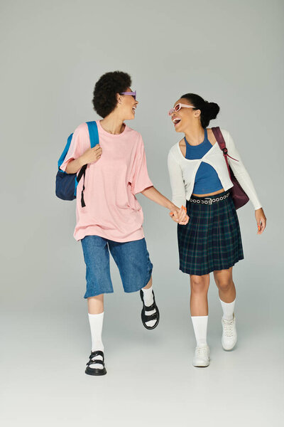 Friends share laughter and style, strolling hand in hand in a playful indoor atmosphere.