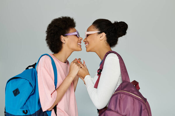 Two friends express their bond with a playful gesture while wearing sunglasses and backpacks.
