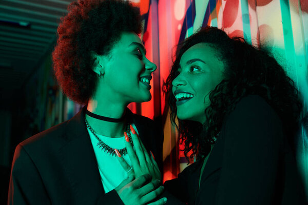 Two friends laugh and connect in a lively, artistic environment full of color and energy.