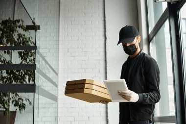 Siyah maskeli bir teslimatçı, yemek kutularını modern ofis ortamlarına taşır..