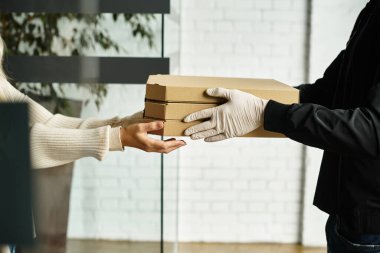 Bir teslimatçı ofis ortamında bir kadına bir paket sunar, güvenlik protokollerini sağlar..