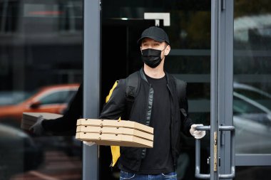 Siyah maskeli bir teslimatçı gün içinde kalabalık bir ofis binasına pizza kutusu getirir..