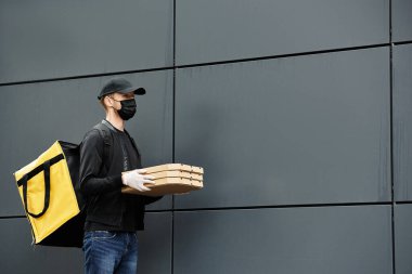 A delivery man wearing a black medical mask brings food orders into an office building while wearing gloves. clipart