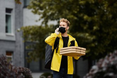 Siyah bir maske takan teslimatçı ofis dışında konuşurken pizza kutuları taşıyor..