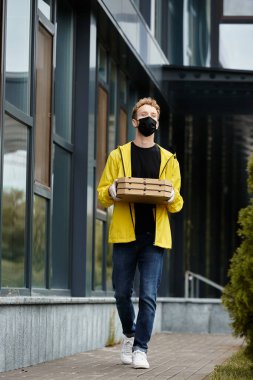 Tıbbi maskeli bir kurye, kalabalık bir ofis binasına pizza kutusu taşıyor..