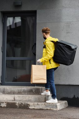 Tıbbi maskeli bir teslimatçı ofis binalarının girişine teslimat için bir paket getiriyor.