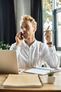 Beyaz tişörtlü düşünceli bir kızıl iş projesiyle meşgul olurken bir ofiste telefon görüşmesi yapıyor..