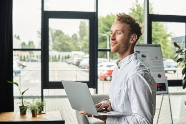 A professional with red hair works intently on a project, displaying focus in a bright office setting. clipart