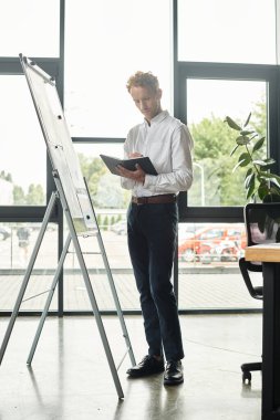 Kendini işine adamış kızıl saçlı bir işadamı, çağdaş bir ofis alanında dururken projesinde işbirliği yapıyor..