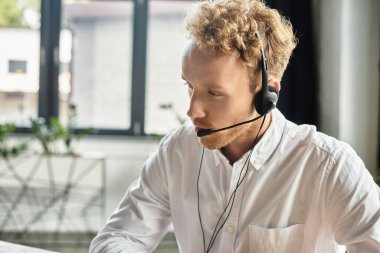 Kızıl saçlı odaklanmış bir işadamı, çağdaş bir ofis ortamında derin düşüncelere dalmış bir projede işbirliği yapıyor..