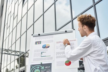 Profesyonel bir kızıl saçlı, proje bulgularını geniş pencereli çağdaş bir ofiste inceliyor..
