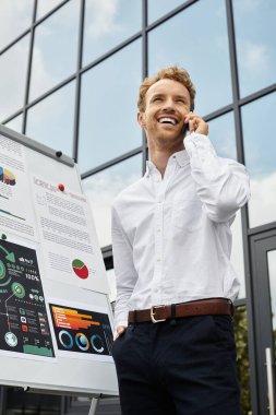 Beyaz gömlekli kızıl saçlı bir işadamı modern bir çalışma alanındaki bir telefon üzerine proje detaylarını tartışıyor..