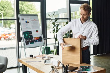 Beyaz tişörtlü kızıl saçlı bir profesyonel, projesinin materyallerini şık bir ofis alanında düzenliyor..