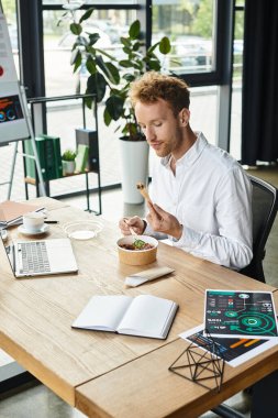 Modern ofis ortamında, kızıl saçlı bir işadamı besleyici bir öğle yemeğinin tadını çıkarırken derin düşüncelere dalmıştır..