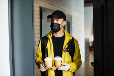 A delivery worker in a black mask brings two coffee cups into a contemporary office space, enhancing productivity. clipart