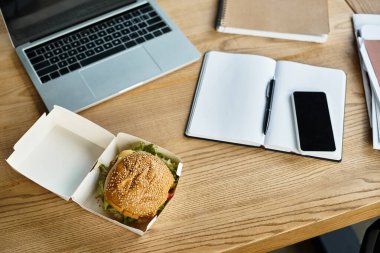 Şık bir ofiste, yemek kabında hamburgerler masanın yanındaki cihazların yanında.