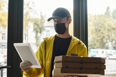 Sarı ceketli ve siyah maskeli bir teslimatçı bir ofis binasına giriyor, elinde birden fazla paket var..