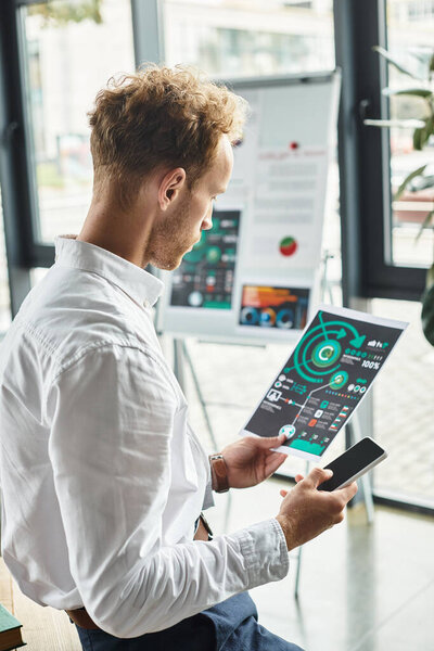 Преданный рыжеволосый бизнесмен изучает метрии проектов, сидя в стильном, современном офисе.