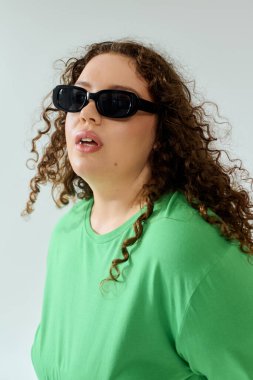 The beautiful woman with curly hair and sunglasses radiates confidence in vibrant green clothing. clipart