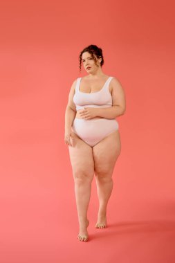 A confident plus size woman showcases her beauty in a pastel pink outfit, posing with grace. clipart