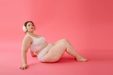 A stunning plus size woman sits gracefully against a vibrant pink backdrop, exuding confidence. clipart