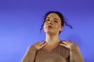 Kendine güveni tam ve cüsseli bir kadın zarif bir şekilde mavi bir arka plana karşı duruyor..