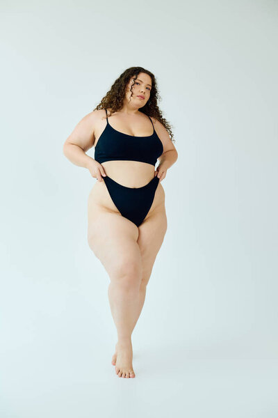 Сияющая уверенность, красивая женщина плюс размер демонстрирует свои изгибы в шикарном черном купальнике.