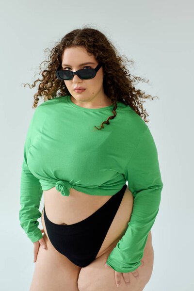 A confident plus size woman showcases her unique style with a vibrant green top and sunglasses.