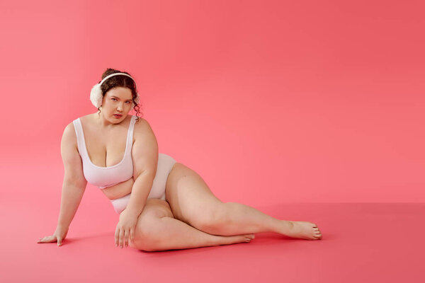 The beautiful plus size woman showcases her elegance while lounging against a bright pink backdrop.