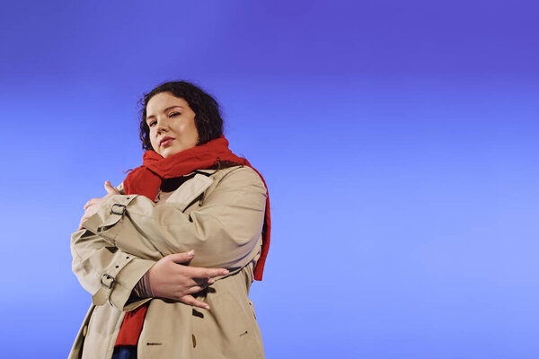 Уверенная женщина плюс размер обнимает свою красоту, стоя на ярком синем фоне.