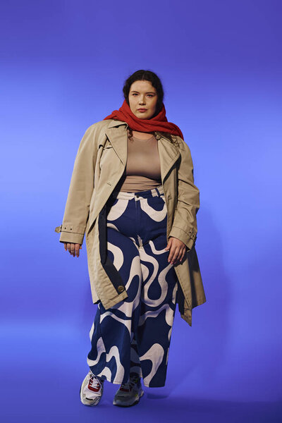 Уверенная женщина в модном наряде стоит на ярком синем фоне, излучающем стиль.